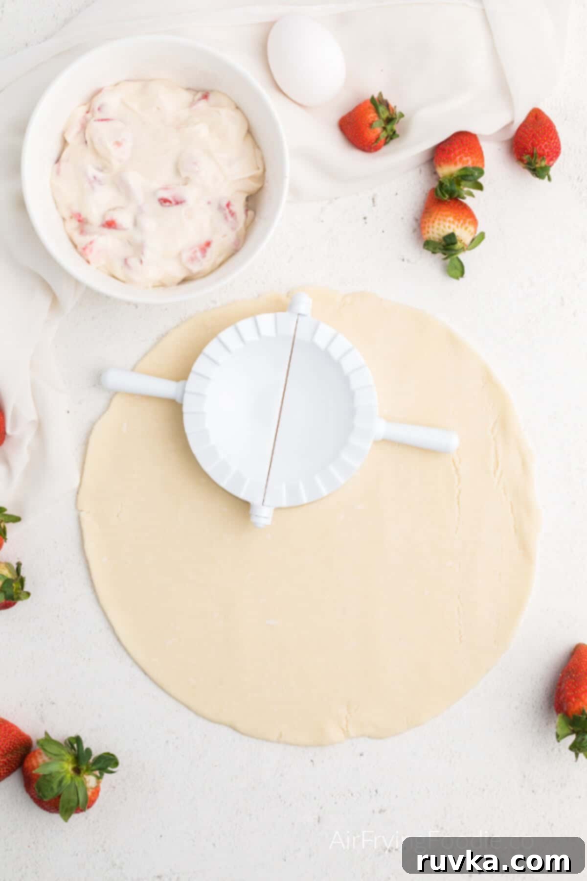 Easy Air Fryer Strawberry Cream Cheese Pie 3 Strawberry cream cheese mixture in a bowl, and a premade pie crust rolled out on the counter, ready to make hand pies.