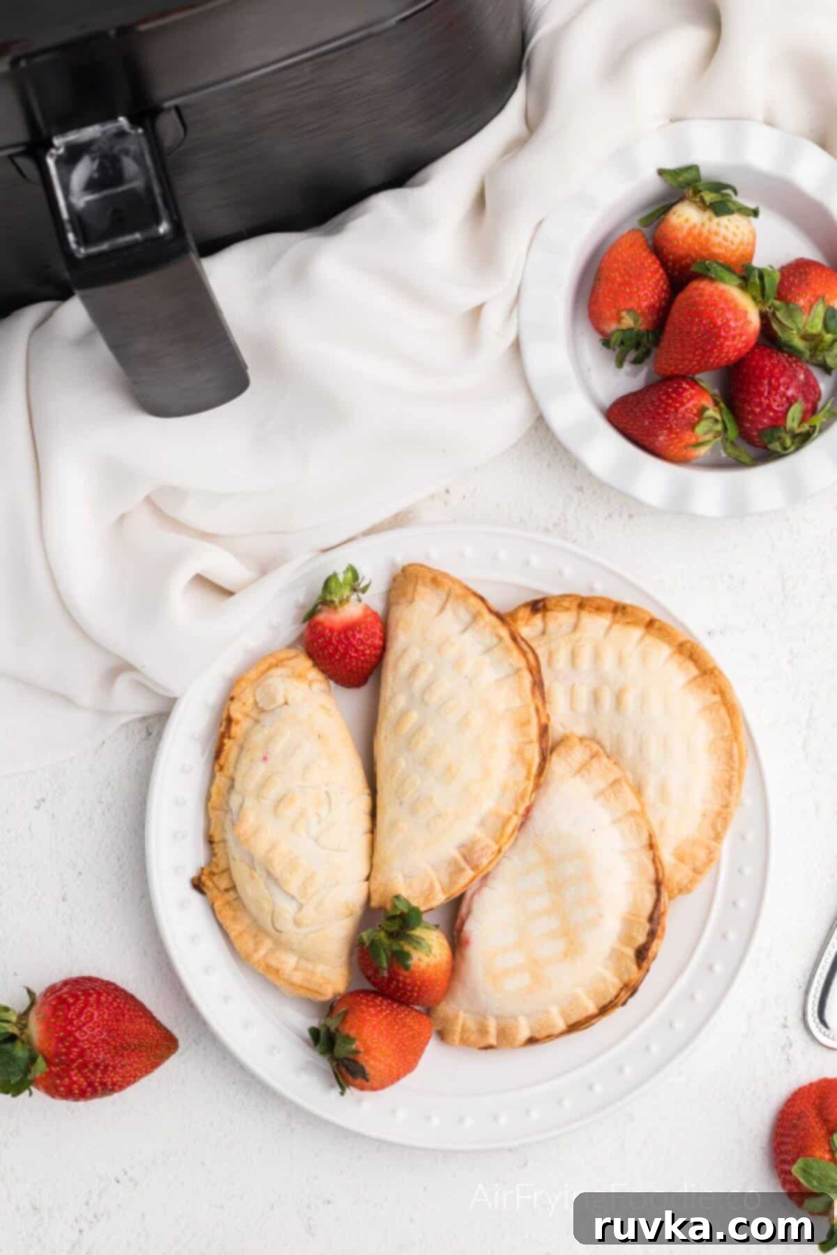 Easy Air Fryer Strawberry Cream Cheese Pie 6 Strawberry cream cheese hand pies made in the air fryer, and served on a white plate.