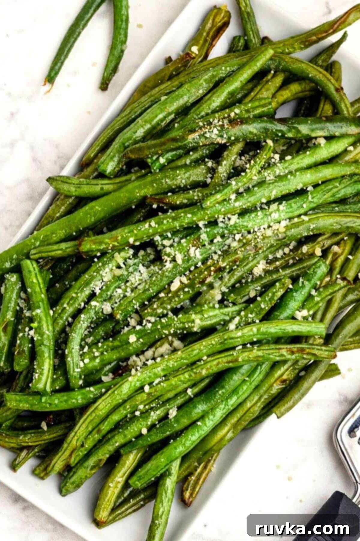 Crispy Air Fried Green Beans 2 Green juicy green beans stacked on a white rectangle plate seasoned and sprinkled with grated parmesan cheese.