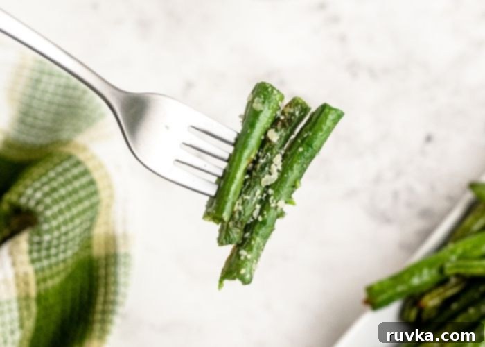 Crispy Air Fried Green Beans 7 Green beans cooked and juicy on a fork after being sprinkled with grated parmesan cheese.