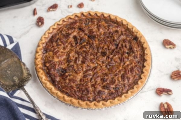 Perfect Air Fryer Pecan Pie 2 Golden brown pecan pie on a pristine white marble table, surrounded by scattered whole pecans, highlighting its irresistible texture.