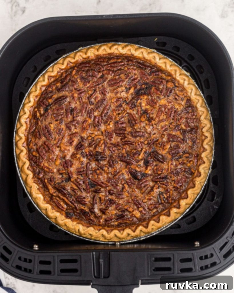 Perfect Air Fryer Pecan Pie 7 A perfectly cooked pecan pie resting in an air fryer basket, showcasing its golden-brown crust and glistening, nutty filling.
