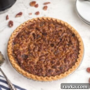 Perfect Air Fryer Pecan Pie 10 Golden pecan pie on a white marble table with scattered pecans around the pie plate, inviting a taste.