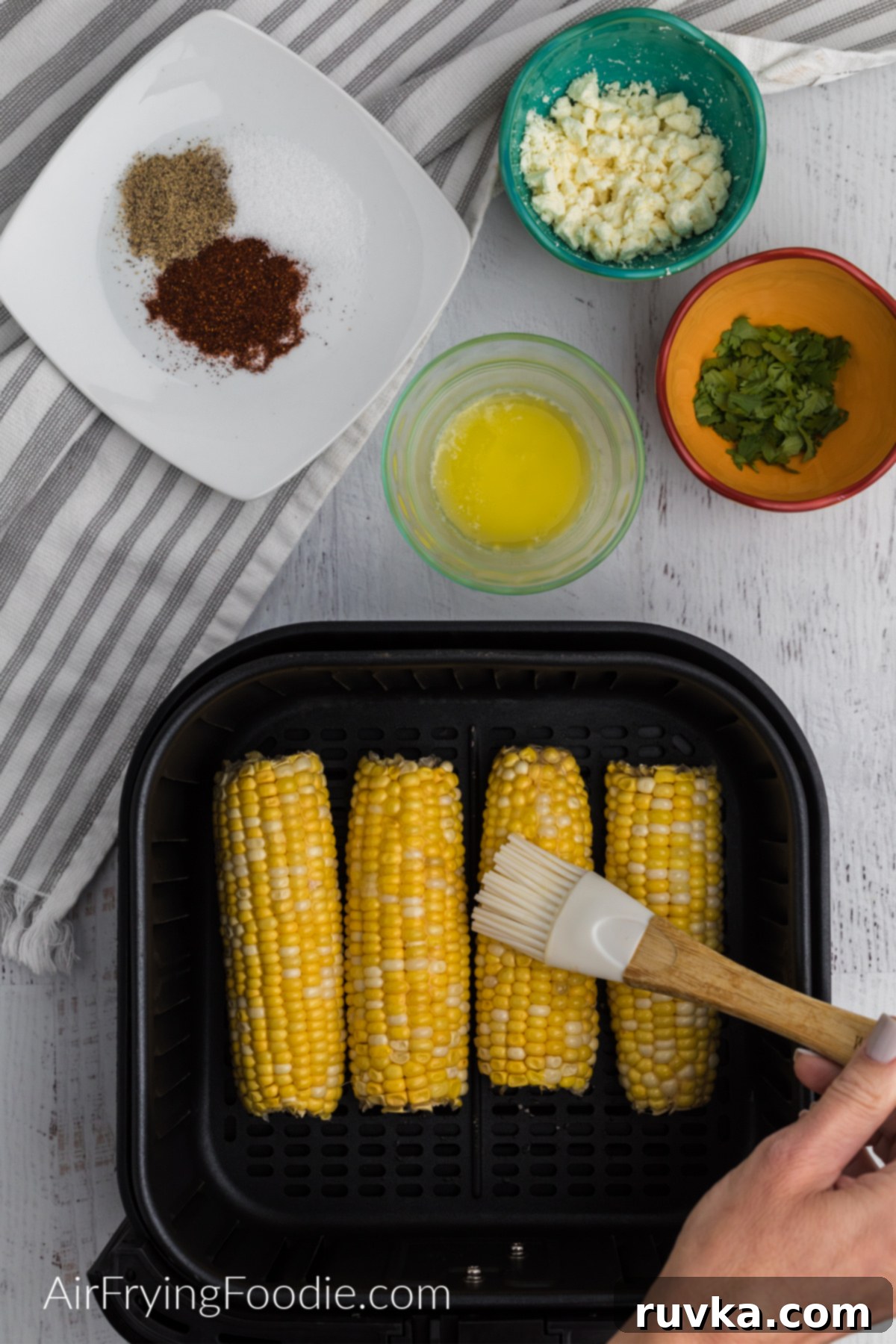 Crispy Air Fryer Elote 4 Brushing butter onto the corn in the air fryer basket.