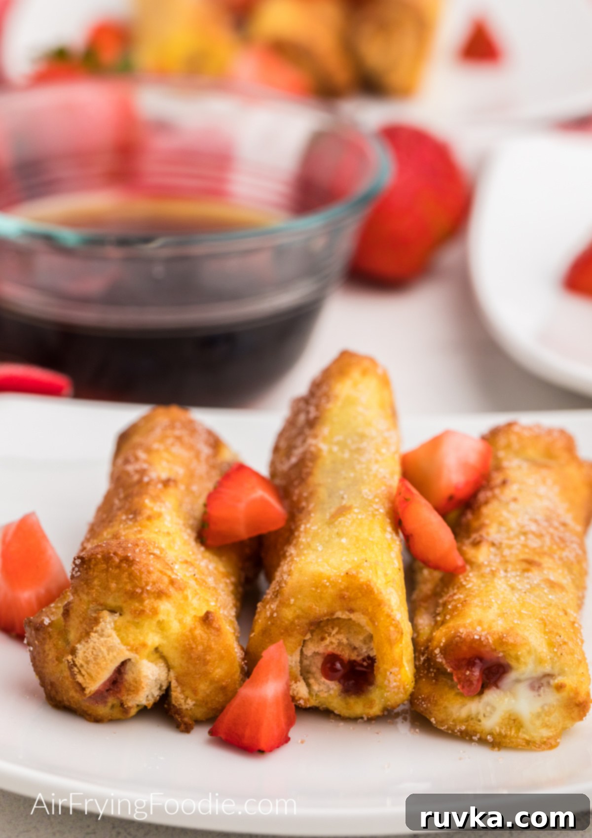 Air Fried Strawberry French Toast Pinwheels 2 Strawberry French Toast Roll Ups made in the air fryer on a white plate topped with fresh strawberries.