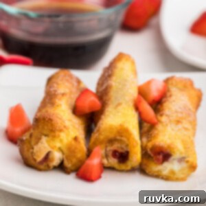 Air Fried Strawberry French Toast Pinwheels 7 Air Fryer Strawberry french toast roll ups on a white plate and garnished with fresh cut strawberries.