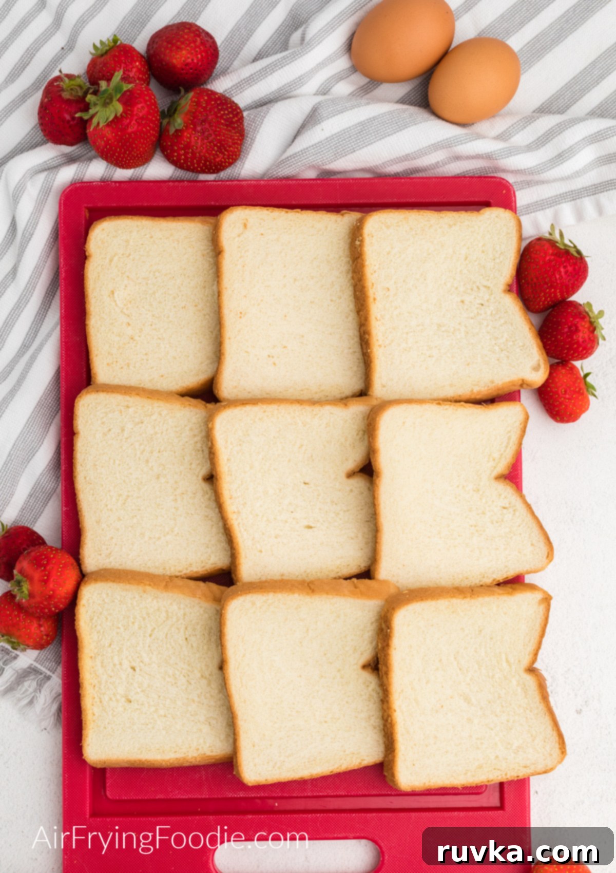 Air Fried Strawberry French Toast Pinwheels 3 bread on a cutting board surrounded by fresh strawberries and eggs.