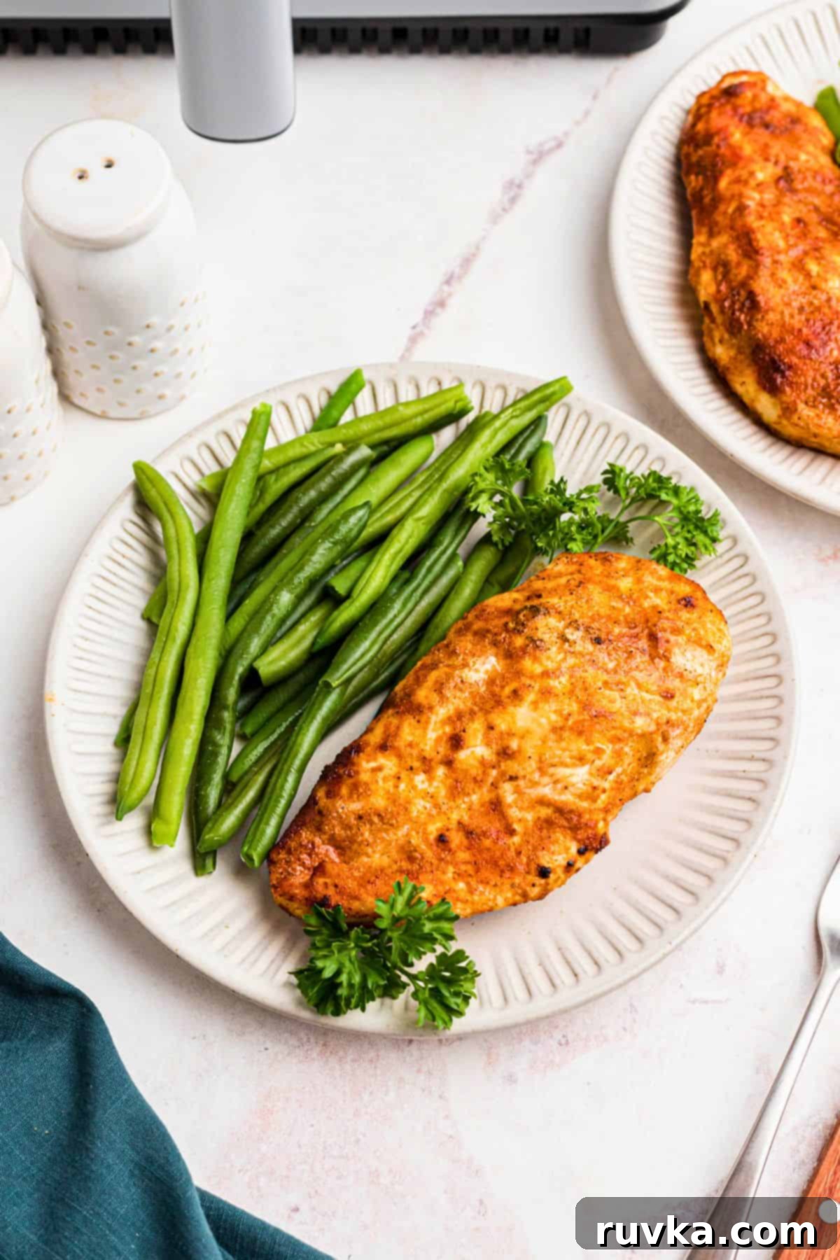 Perfect Air Fryer Chicken Breast 2 Golden juicy chicken breast on a white plate with green beans on a marble table.