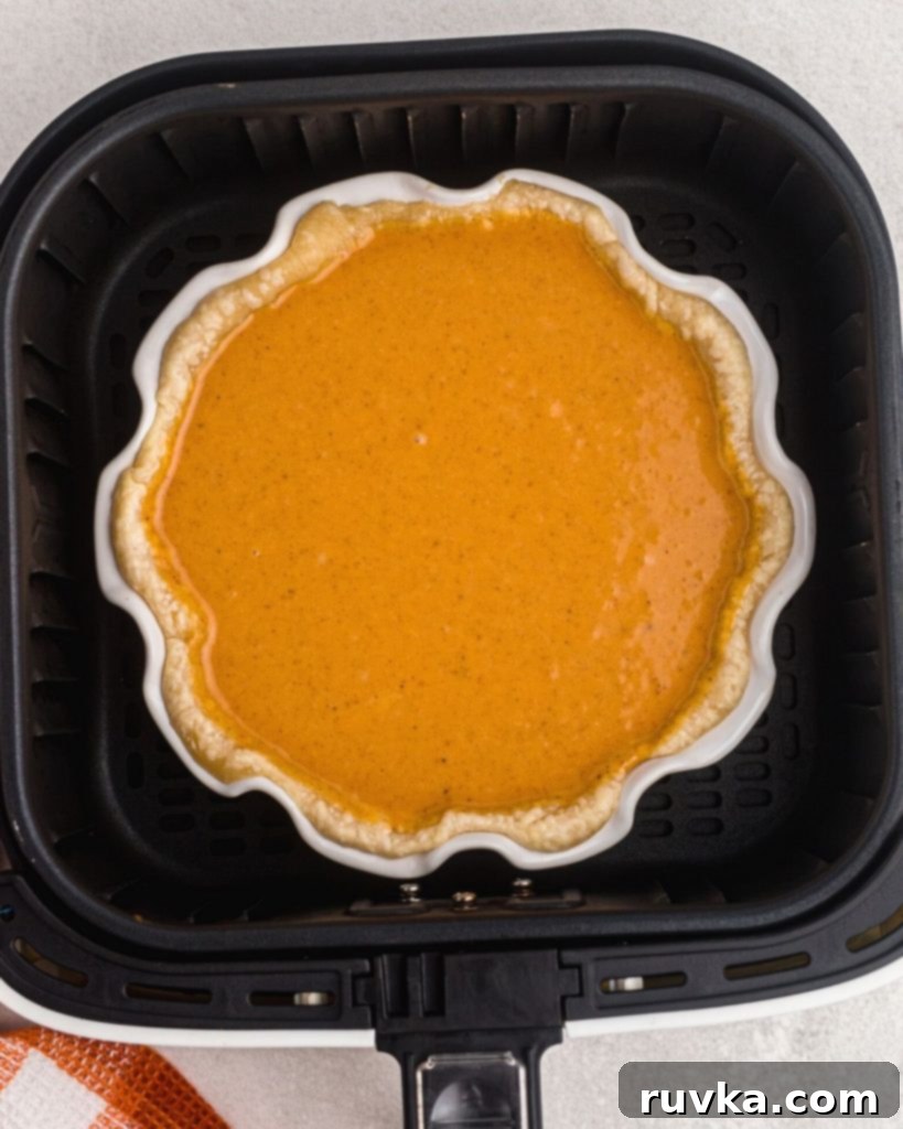 Air Fryer Pumpkin Pie 6 Uncooked pumpkin pie in an air fryer basket.