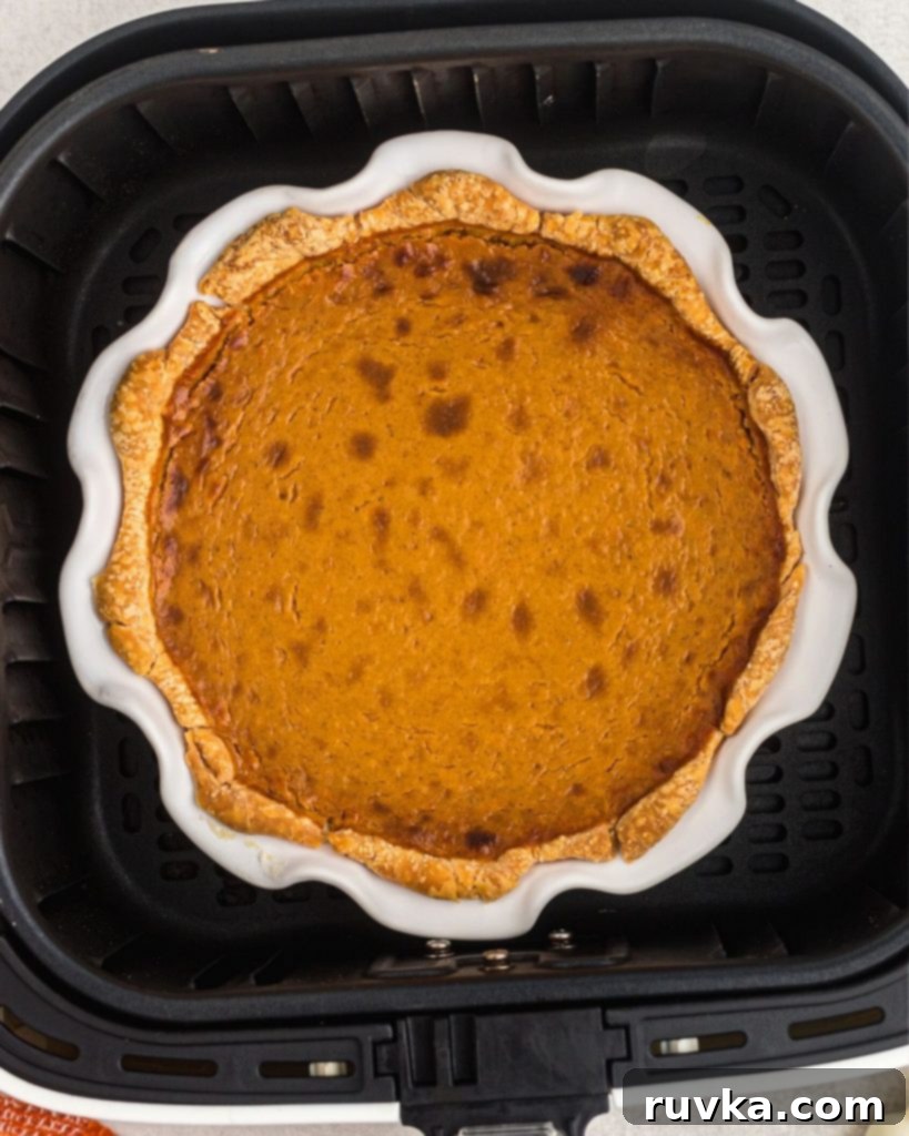 Air Fryer Pumpkin Pie 7 Baked pumpkin pie in a white pie plate in an air fryer basket.