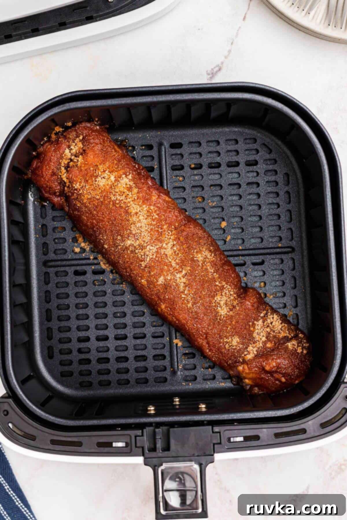 Tender Air Fryer Pork Tenderloin in a Flash 7 Uncooked seasoned pork tenderloin in the air fryer basket.