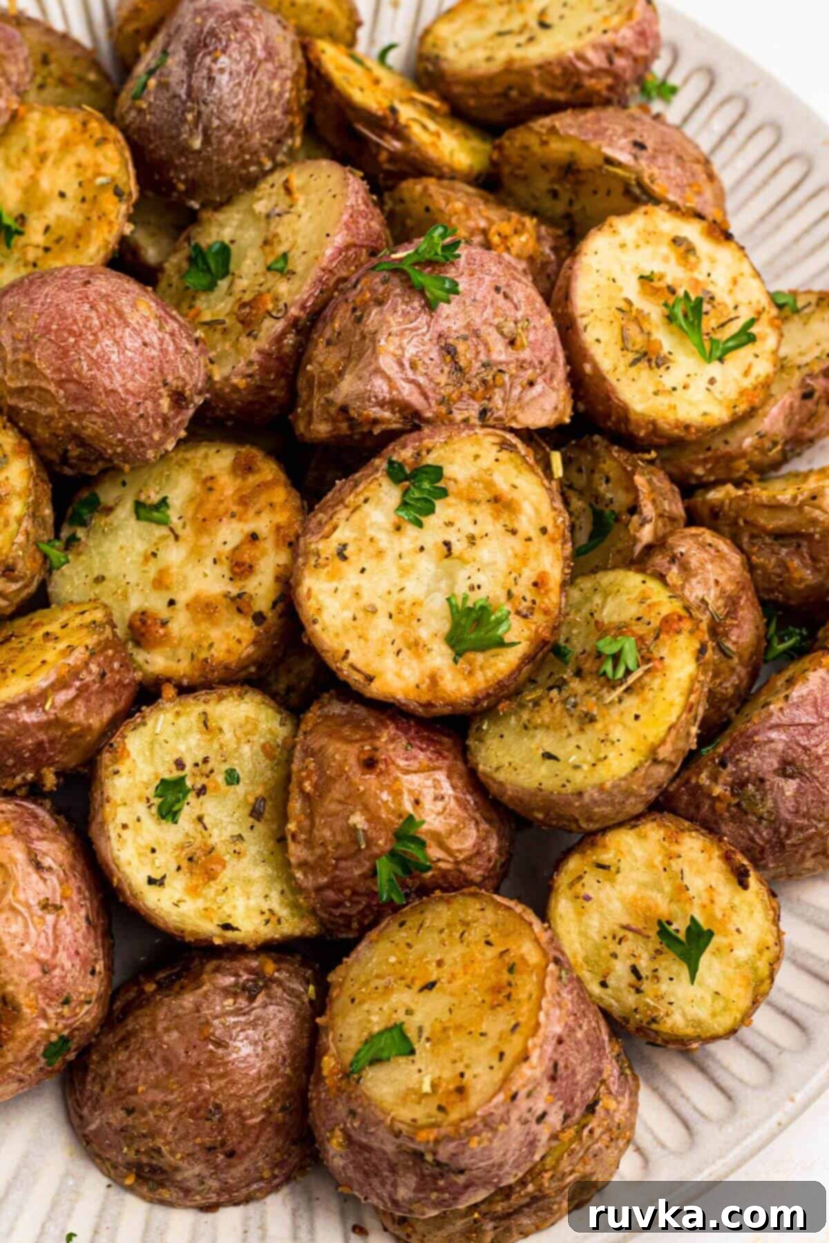 Crispy Air Fryer Potatoes 2 Golden brown seasoned baby potatoes on a white plate after being cooked in the air fryer.