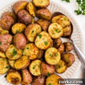 Crispy Air Fryer Potatoes 9 Golden crispy seasoned baby potatoes on a white plate with a serving spoon in the corner of the plate.