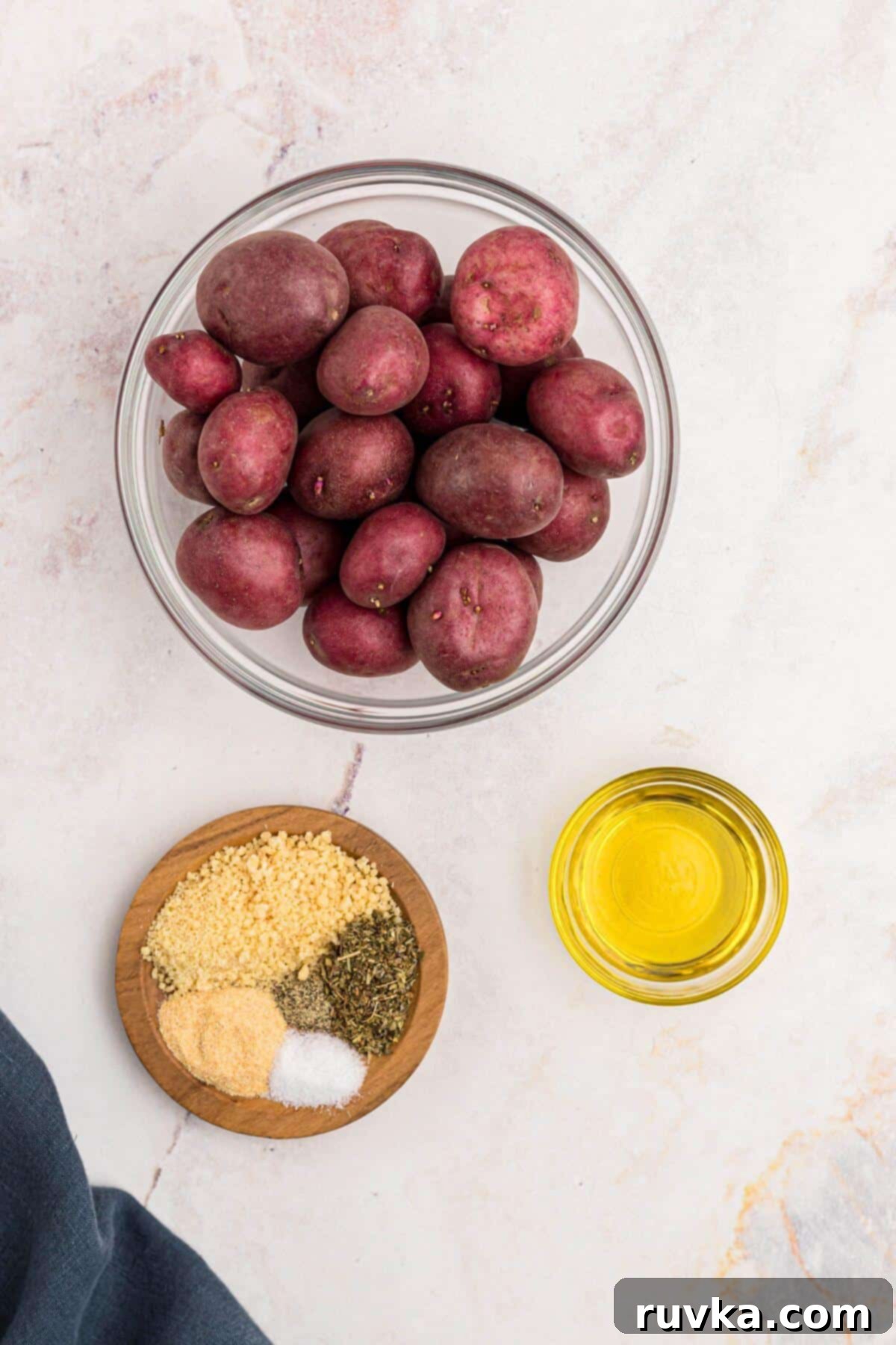 Crispy Air Fryer Potatoes 3 Uncooked red baby potatoes in a clear glass bowl with olive oil, seasonings and parmesan cheese on a marble table.