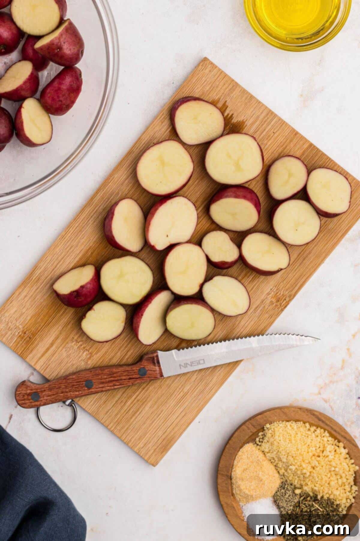 Crispy Air Fryer Potatoes 4 Baby red potatoes being cut in half on a wooden cutting board.