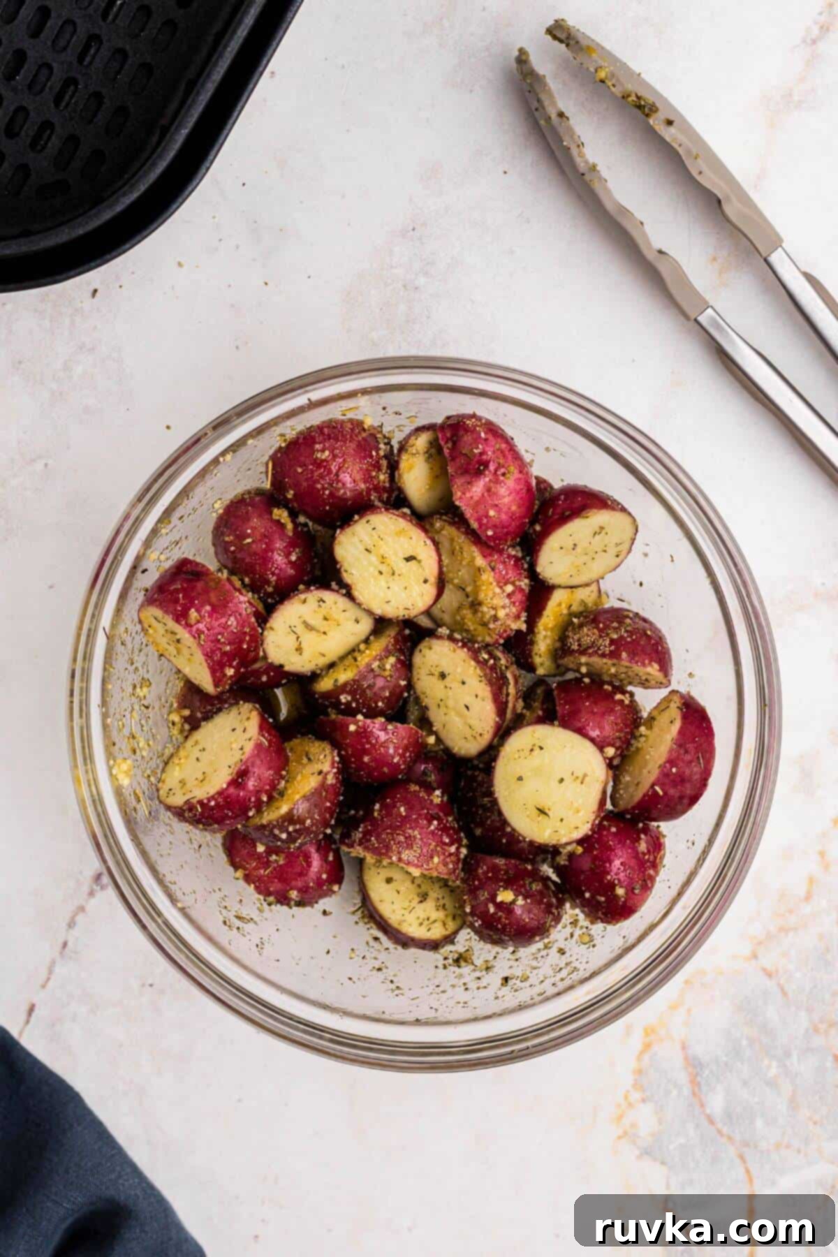 Crispy Air Fryer Potatoes 5 Red baby potatoes in a clear glass bowl after being tossed with olive oil, seasonings, and parmesan cheese.