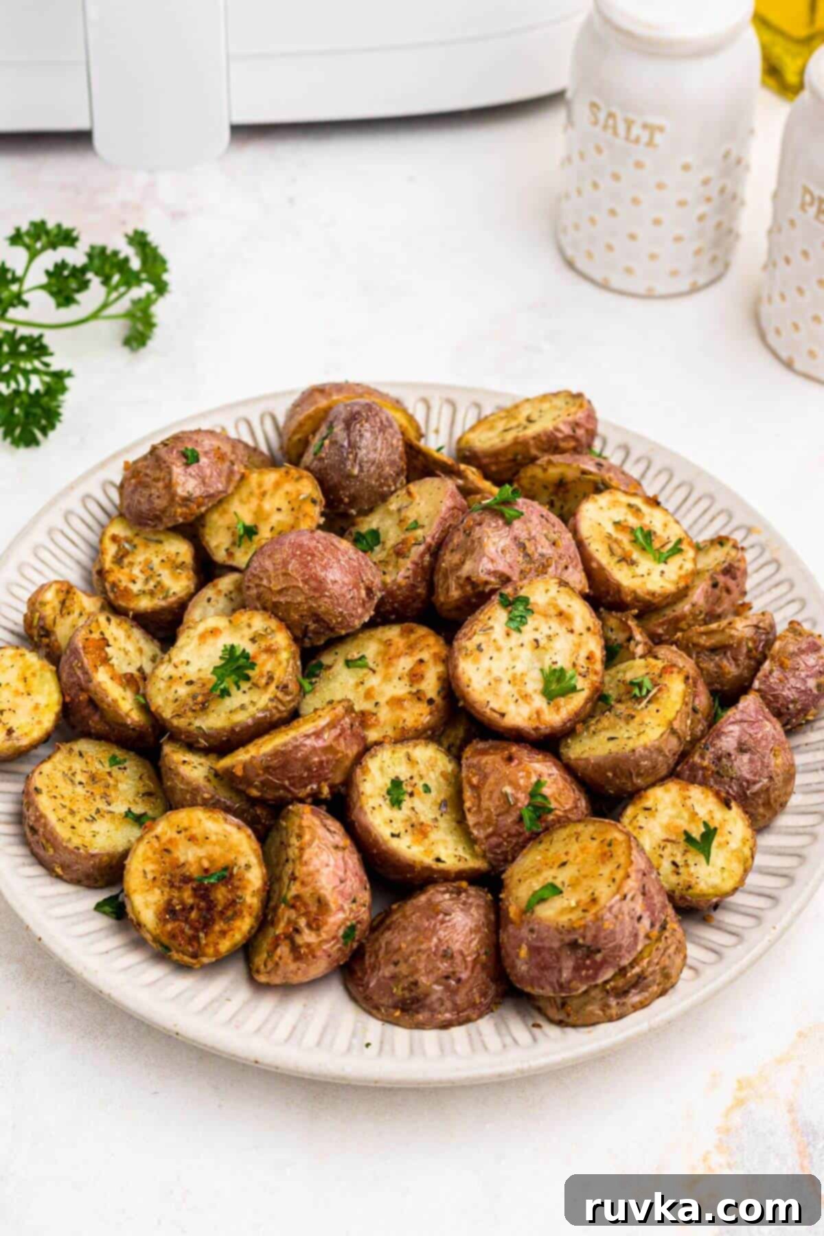 Crispy Air Fryer Potatoes 8 Baby red potatoes sliced in half and cooked until golden brown with seasonings, stacked on a white plate.