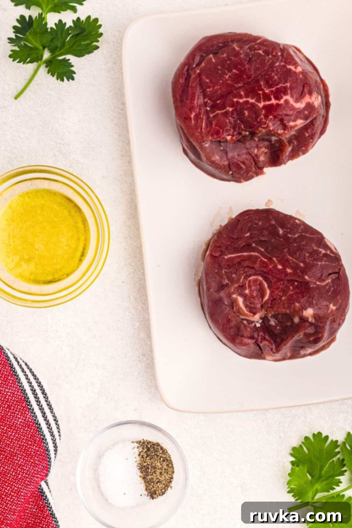 Perfect Air Fryer Filet Mignon 3 Uncooked filets, olive oil, and salt and pepper on a marble table.