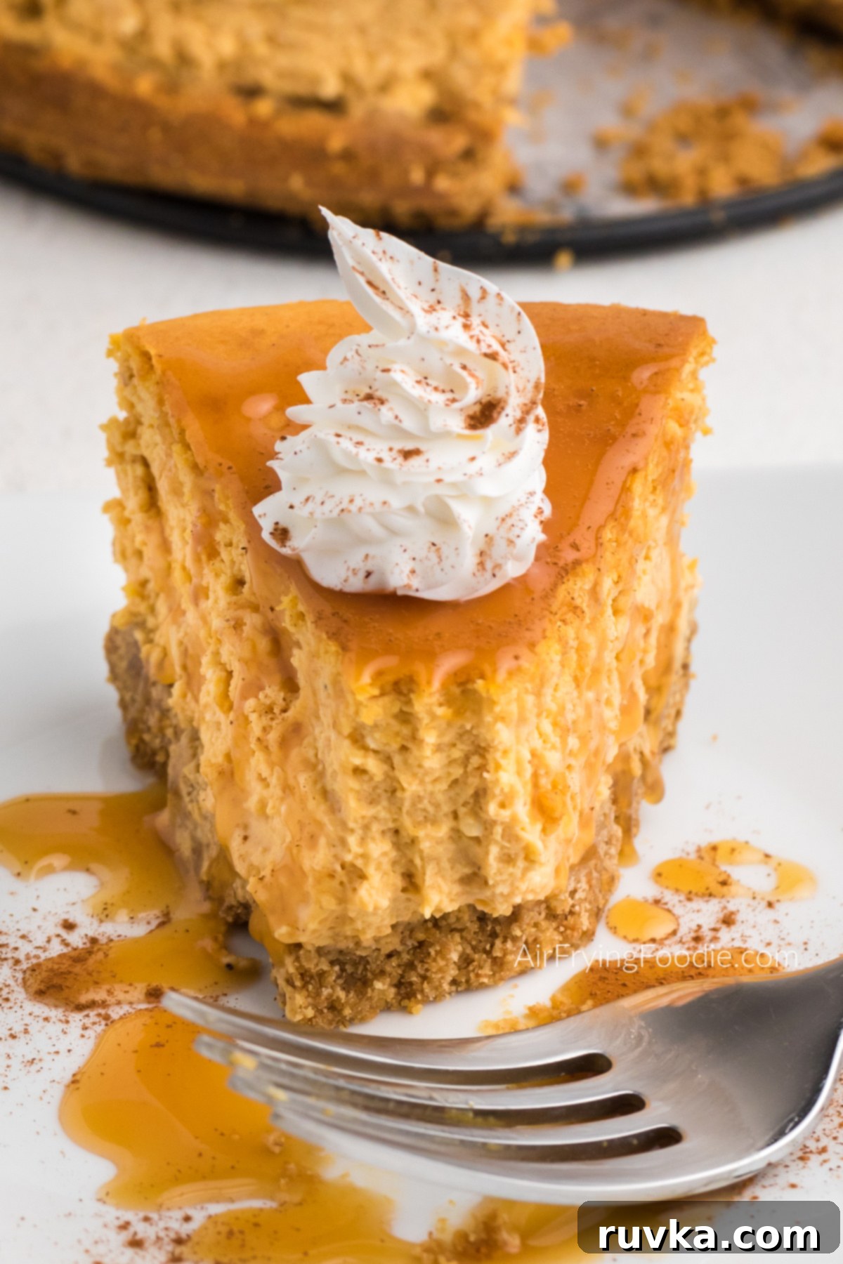 Air Fryer Pumpkin Cheesecake 2 Slice of air fryer pumpkin cheesecake on a plate with a bite missing.