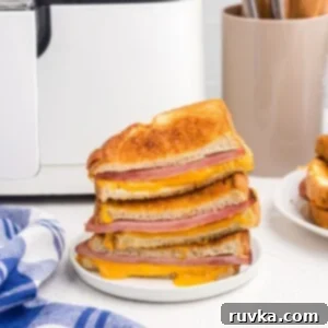 Air Fryer Golden Ham and Cheese Melt 8 Close up photo of ham and cheese sandwiches, golden and with melted cheese dripping out onto plate.