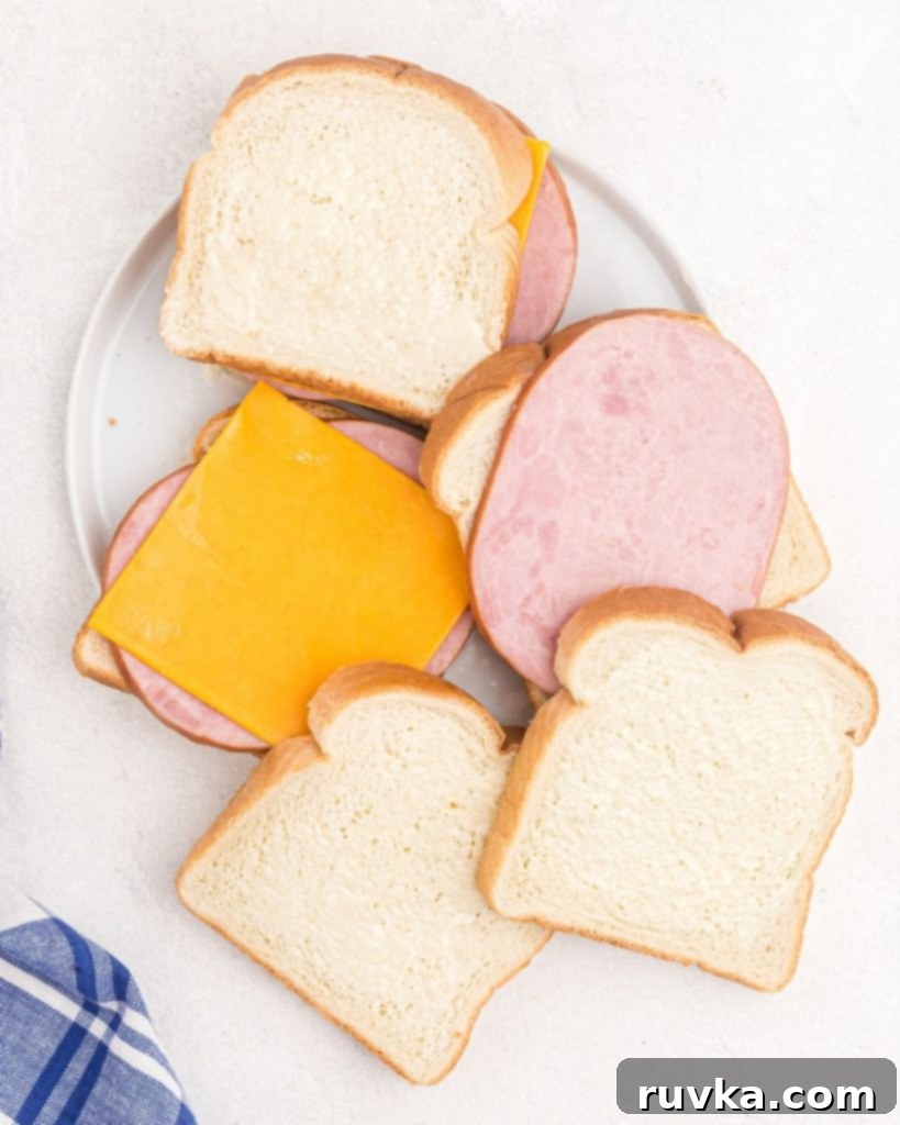 Air Fryer Golden Ham and Cheese Melt 4 Slices of buttered bread with ham and cheese slices being stacked onto a plate.