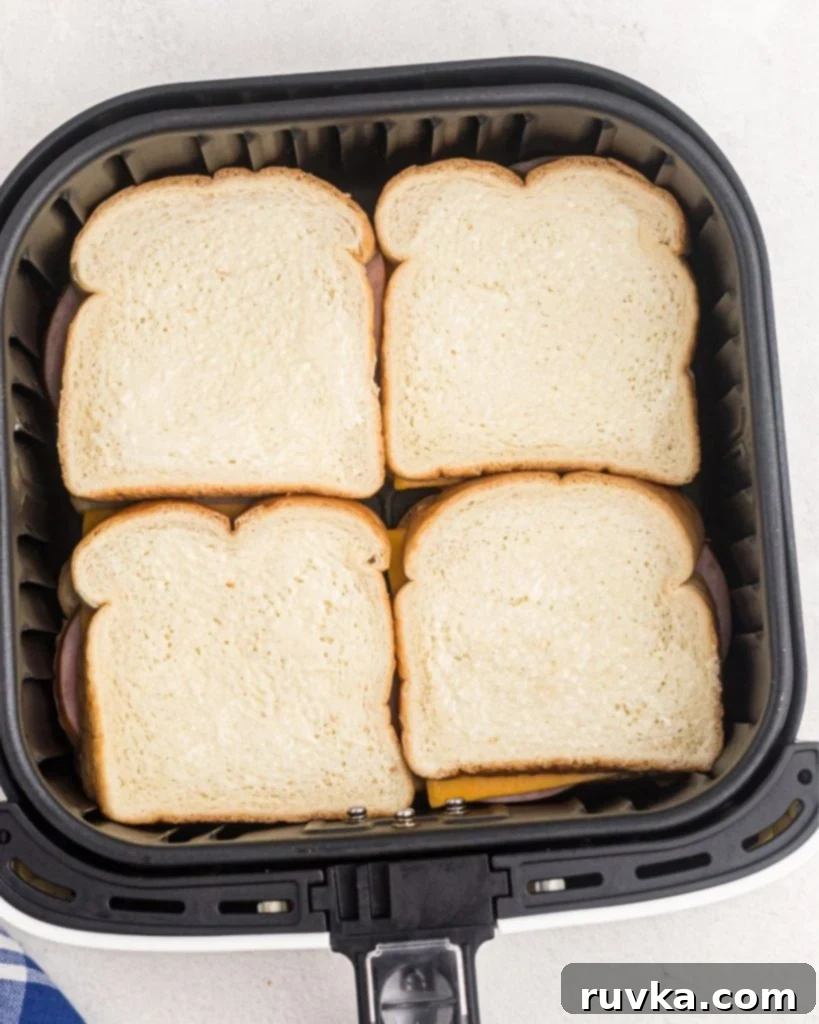 Air Fryer Golden Ham and Cheese Melt 5 Four butter ham and cheese sandwiches in an air fryer basket before being cooked.