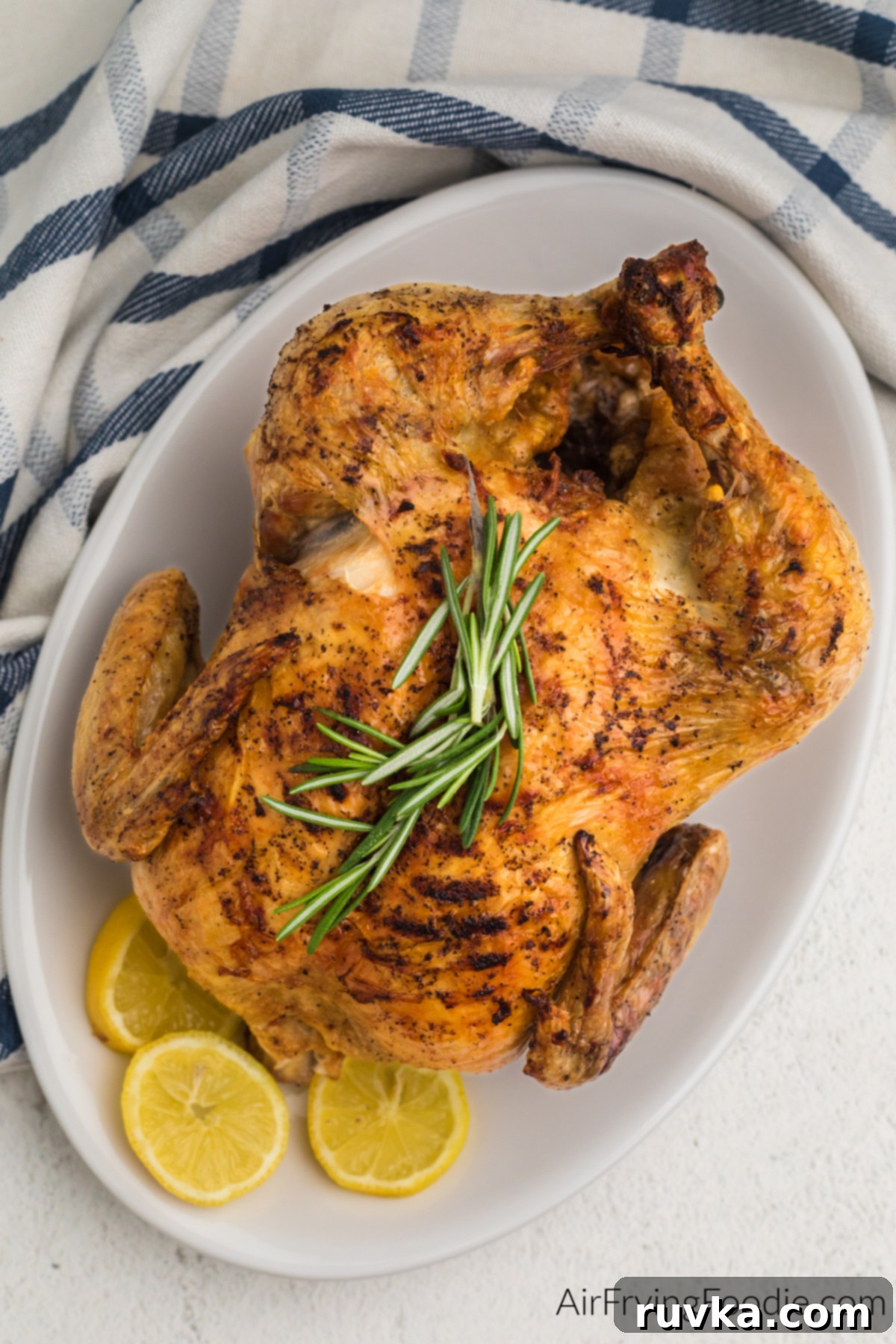Crispy Air Fryer Whole Chicken 2 Air fried whole chicken on a white serving plate with sprigs of rosemary and lemon slices.