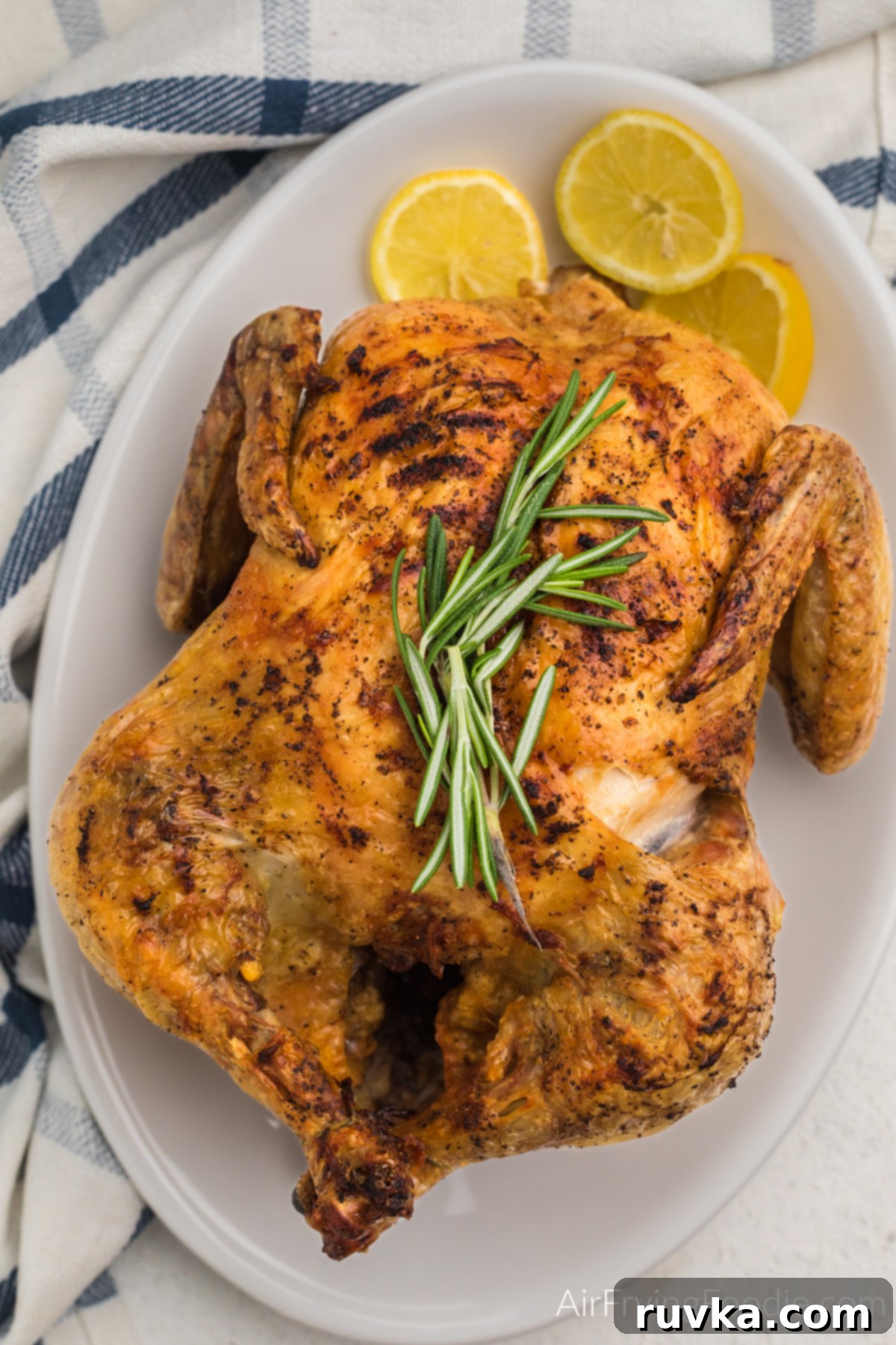 Crispy Air Fryer Whole Chicken 6 Air fried whole chicken on a serving plate with rosemary sprigs on the top and served with lemon slices.