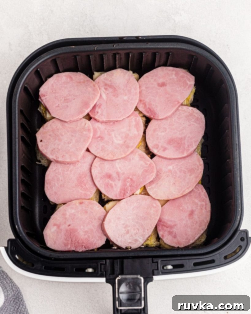 Irresistible Air Fryer Ham and Cheese Sliders 6 The bottom halves of Hawaiian rolls in an air fryer basket, now layered with ham slices on top of the cheese, perfectly prepped.