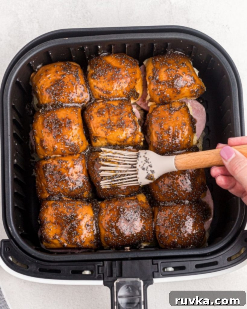 Irresistible Air Fryer Ham and Cheese Sliders 7 Hawaiian rolls assembled in the air fryer basket, being carefully brushed with the flavorful poppyseed glaze, enhancing their golden potential.