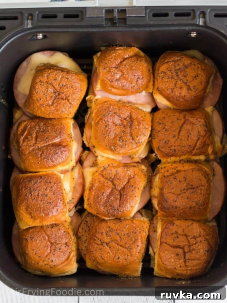 Irresistible Air Fryer Ham and Cheese Sliders 8 Freshly cooked ham and cheese sliders in the air fryer basket, with golden-brown tops and melted cheese, ready for serving.