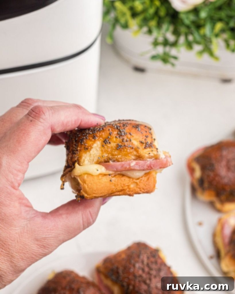 Irresistible Air Fryer Ham and Cheese Sliders 10 A hand holding up a single, perfectly golden air fryer ham and cheese slider, showcasing its melted cheese and delicious crust.