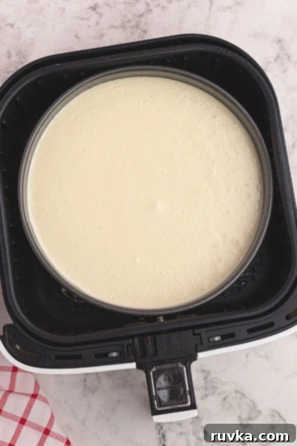 Effortless Air Fryer Cheesecake 3 Uncooked cheesecake in a springform pan, carefully placed inside the basket of an air fryer, ready for cooking.