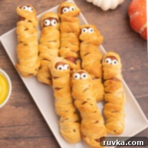 Spooky Air Fryer Hot Dog Mummies 10 Golden crusted and wrapped hot dogs, designed to look like mummies with whimsical candy eyes, a perfect Halloween snack.