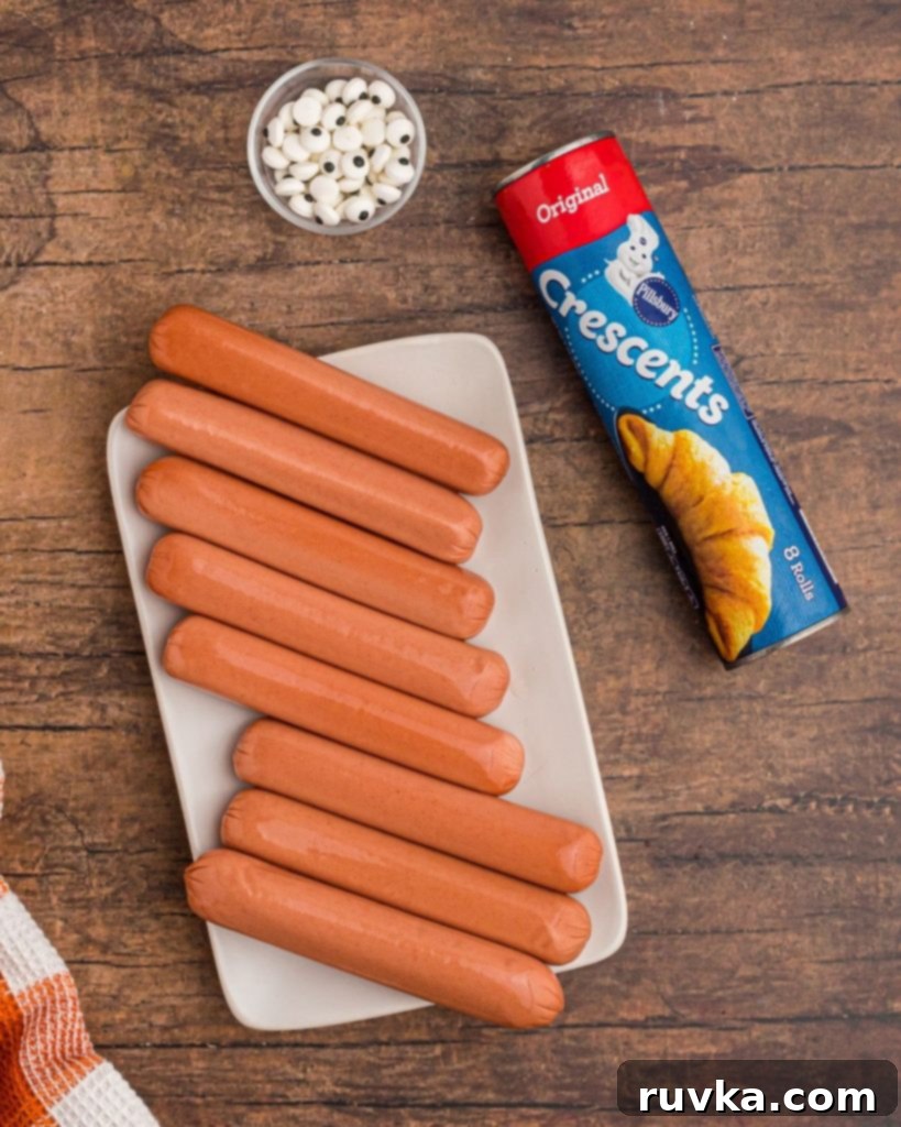 Spooky Air Fryer Hot Dog Mummies 4 The simple ingredients laid out: a package of hot dogs, a can of crescent roll dough, and a container of candy eyes, ready to be assembled into Air Fryer Mummy Dogs.