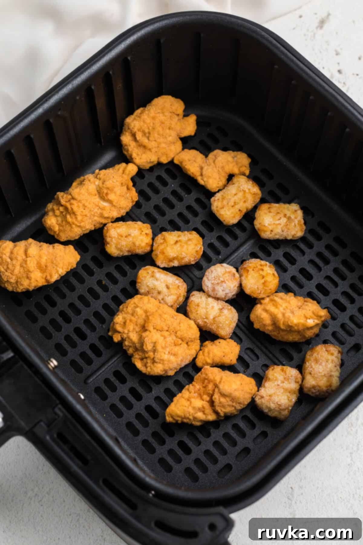 Crispy Air Fryer Breakfast Bowl 4 chicken nuggets and tater tots in air fryer basket cooking for the breakfast bowl.