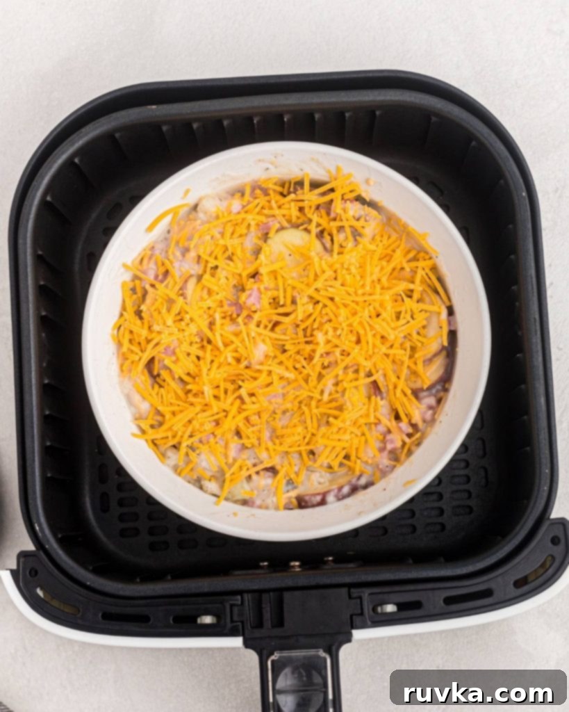 Air Fryer Golden Ham and Potato Bake 5 Baking dish filled with uncooked ham and potato casserole, topped with cheese, placed inside an air fryer basket, ready to cook.