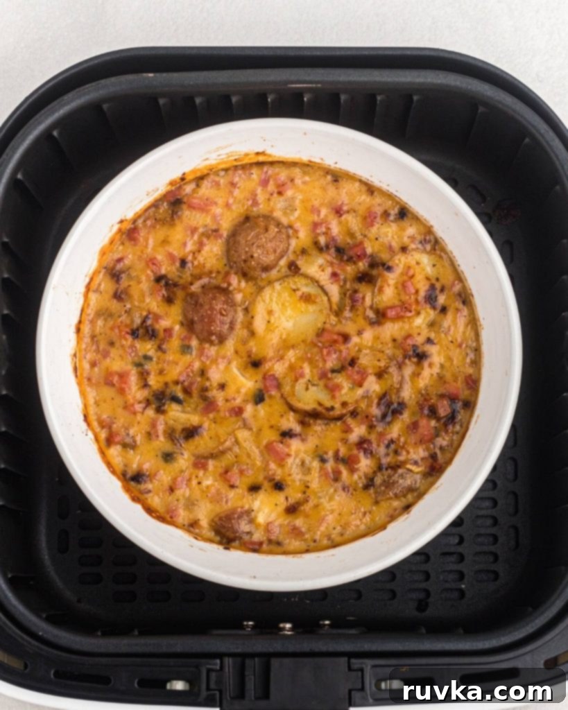 Air Fryer Golden Ham and Potato Bake 6 Cooked air fryer ham and potato casserole, hot and bubbly with melted cheese, resting inside the air fryer basket.