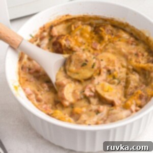 Air Fryer Golden Ham and Potato Bake 8 Spoonful of cheesy ham and potatoes in a white dish, showcasing the golden melted cheese and creamy texture.