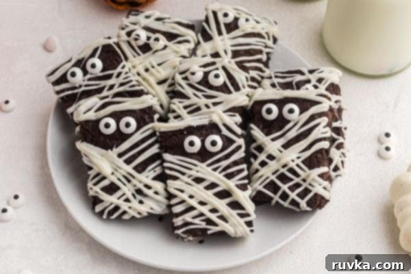 Halloween Air Fryer Mummy Brownies 2 Plate of mummy brownies stacked on a white plate with candy eyes scattered on the table.