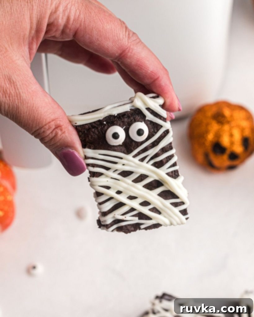 Halloween Air Fryer Mummy Brownies 9 Hand holding brownie mummy with candy eyeballs in front of air fryer.