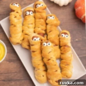 Spooktacular Air Fryer Charcuterie Board 4 Golden-crusted hot dogs wrapped in crescent roll strips to resemble mummies, adorned with candy eyes for a fun Halloween snack.