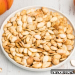 Crispy Air Fryer Pumpkin Seeds 6 Roasted air fryer pumpkin seeds on a white plate sprinkled with cinnamon, salt, and brown sugar.