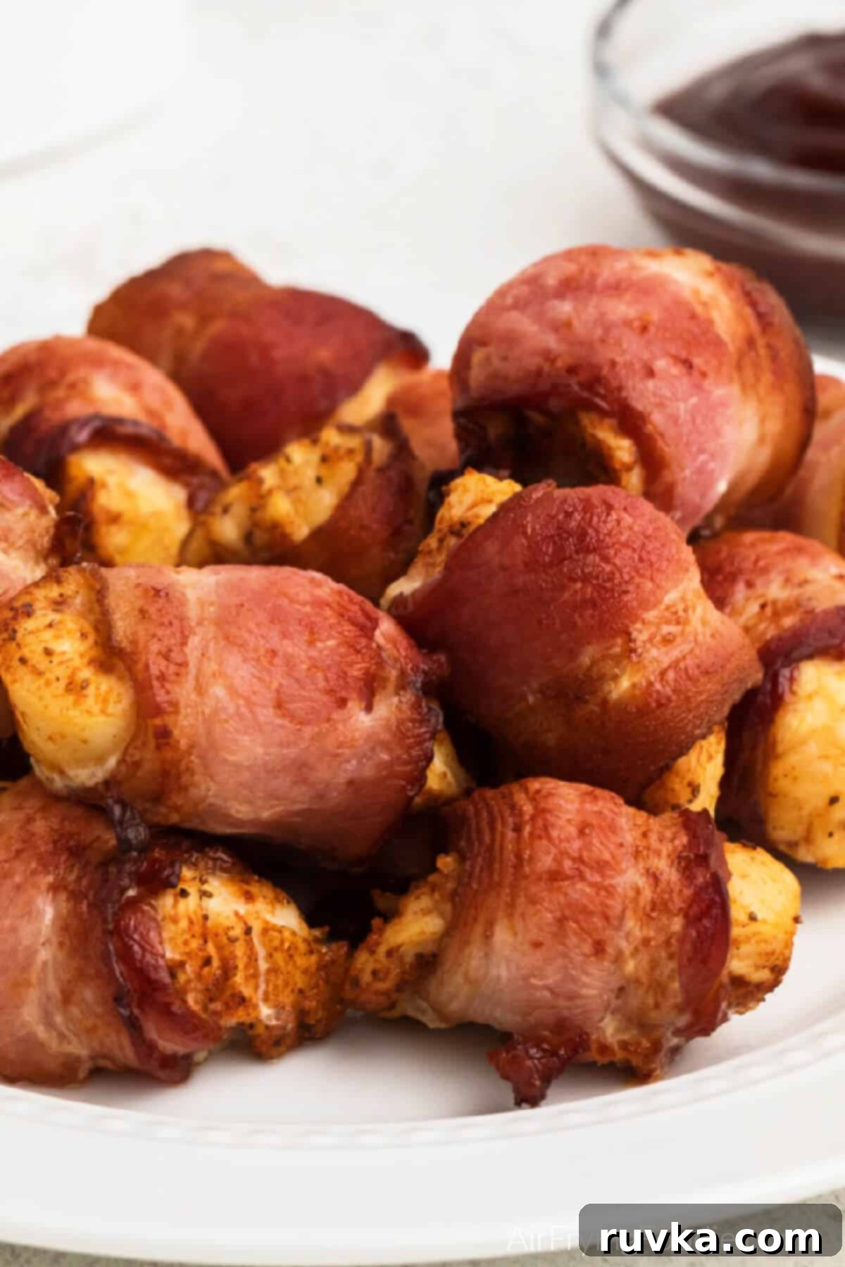 Perfectly Crispy Air Fryer Bacon Wrapped Chicken Bites 2 Bacon wrapped chicken bites made in the air fryer and served on a white plate.