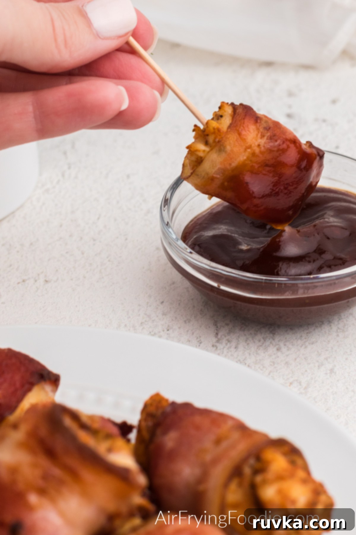 Perfectly Crispy Air Fryer Bacon Wrapped Chicken Bites 3 Bacon wrapped chicken bites being dipped in BBQ sauce.