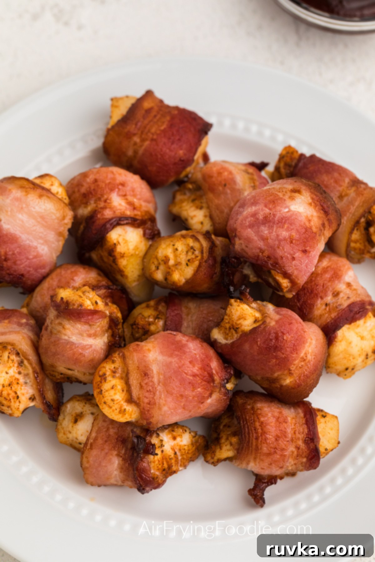 Perfectly Crispy Air Fryer Bacon Wrapped Chicken Bites 6 Bacon wrapped chicken bites on a white plate ready to serve.