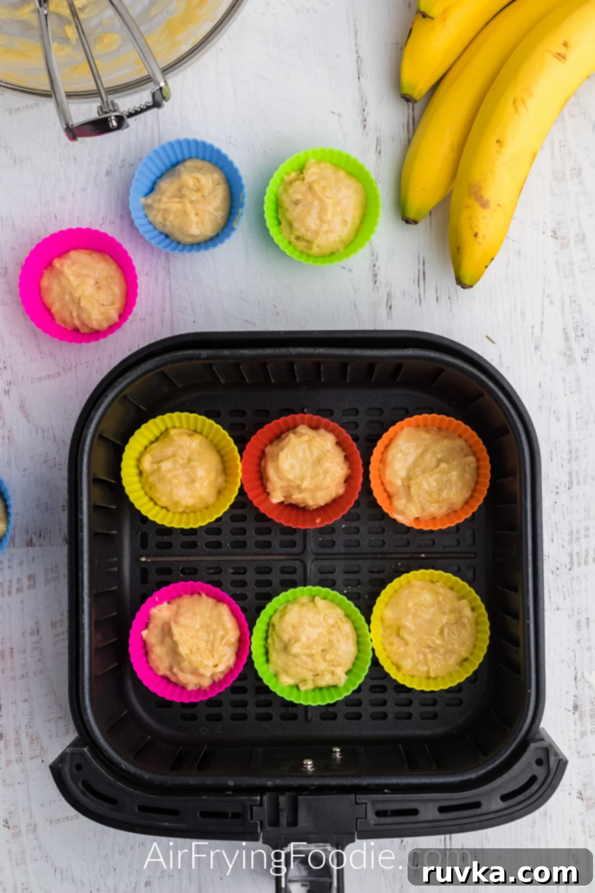 Easy Air Fryer Banana Muffins 5 Banana muffin batter in silicone cups in the basket of the air fryer.