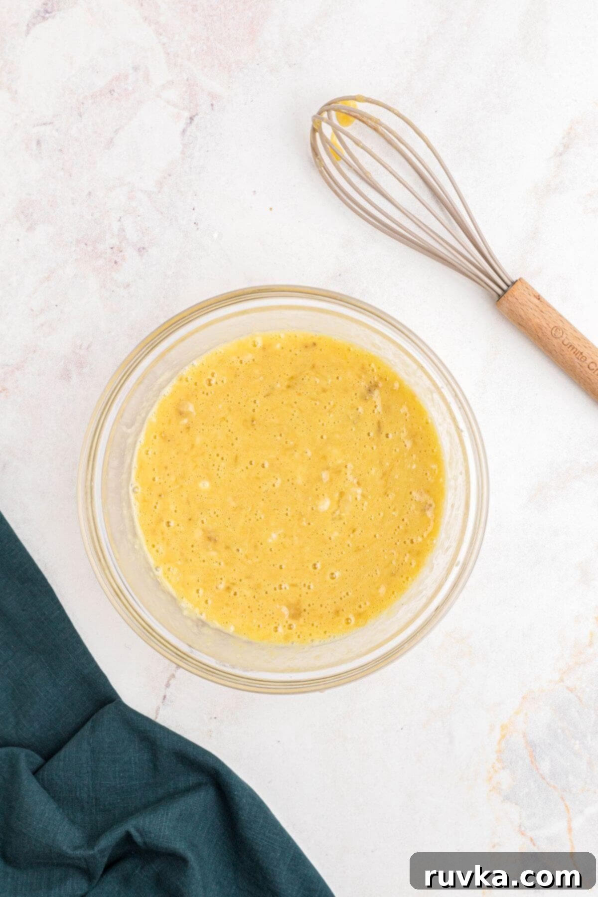 Mashed bananas mixed with eggs and other ingredients, in a clear glass bowl. 