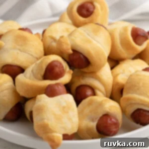 Golden Air-Fried Sausage Bites 7 Close up photo of air fryer pigs in a blanket on a white plate ready to be served, showcasing the perfectly baked crescent rolls.