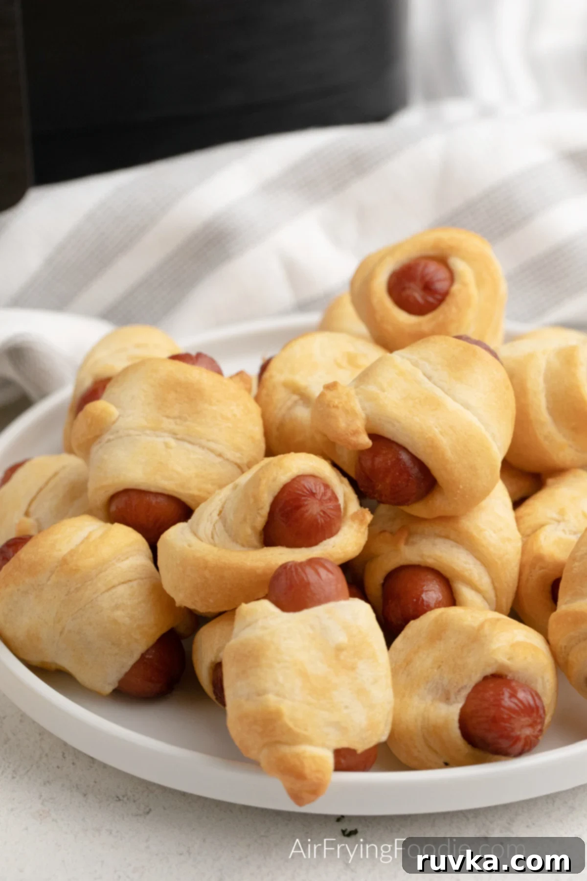 Golden Air-Fried Sausage Bites 3 Pigs in a Blanket made in the air fryer with the air fryer in the background, showcasing the ease of preparation.